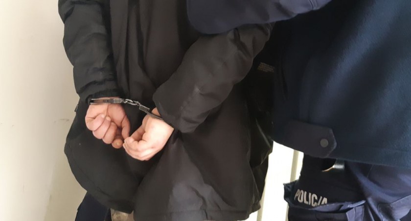 Zdjęcie zatrzymanego mężczyzny w kajdankach prowadzonego przez policjanta/ podlaska.policja.gov.pl