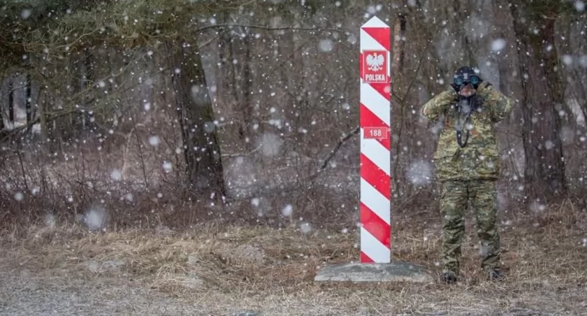 Zdjęcie strażnika granicznego patrzącego przez lornetkę przy słupie granicznym/ Straż Graniczna